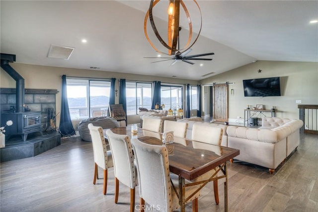 dining space featuring hardwood / wood-style floors, a wood stove, ceiling fan, and lofted ceiling