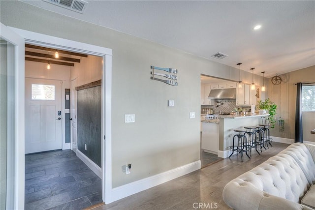 interior space featuring pendant lighting, white cabinets, beamed ceiling, a kitchen bar, and kitchen peninsula