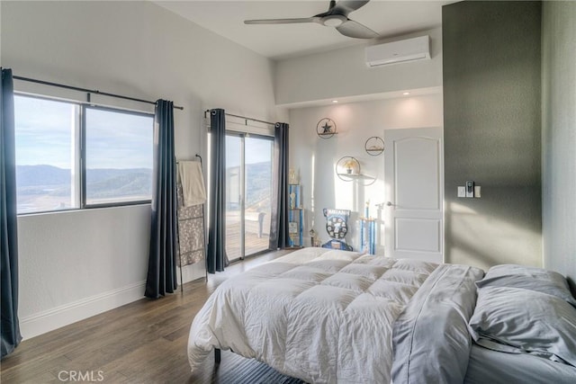 bedroom featuring ceiling fan, a wall mounted AC, a mountain view, hardwood / wood-style floors, and access to outside