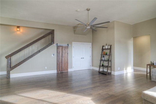 unfurnished living room featuring a barn door, ceiling fan, and dark wood-type flooring