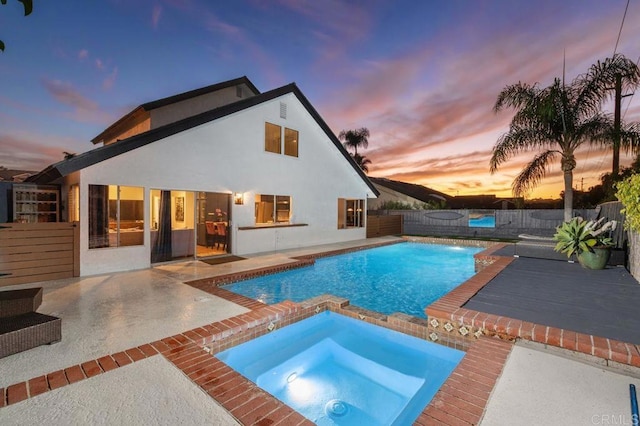 pool at dusk with a patio area and an in ground hot tub