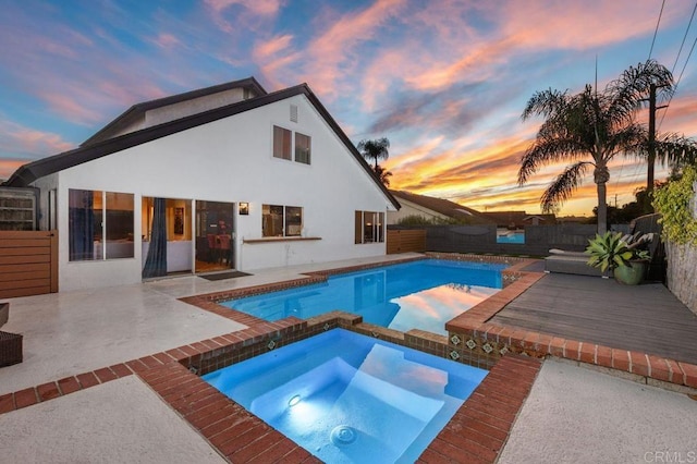 pool at dusk featuring an in ground hot tub and a wooden deck