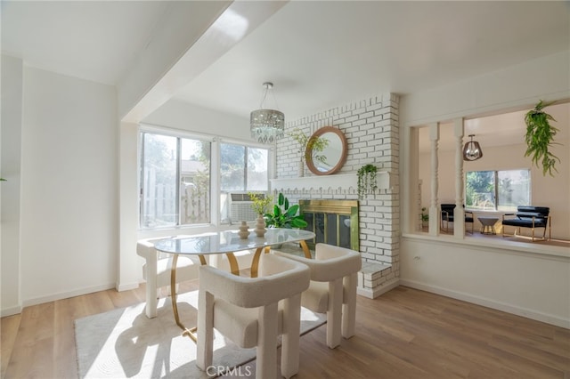 dining room featuring wood-type flooring, a brick fireplace, and a notable chandelier