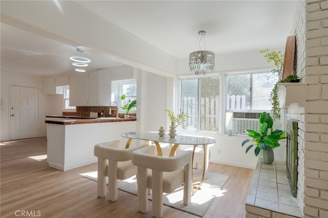 dining room featuring a brick fireplace, a notable chandelier, sink, and light hardwood / wood-style flooring