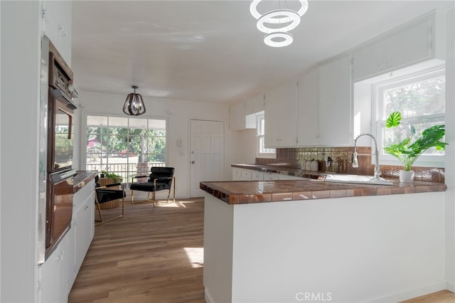 kitchen featuring a healthy amount of sunlight, white cabinetry, kitchen peninsula, and light hardwood / wood-style flooring