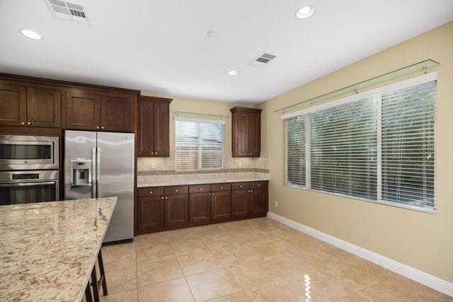 kitchen featuring light stone countertops, appliances with stainless steel finishes, tasteful backsplash, dark brown cabinets, and light tile patterned flooring