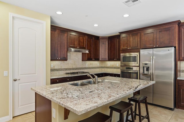 kitchen featuring a kitchen breakfast bar, a kitchen island with sink, light stone countertops, and stainless steel appliances