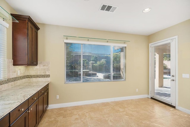 kitchen with dark brown cabinets, light tile patterned flooring, light stone counters, and tasteful backsplash