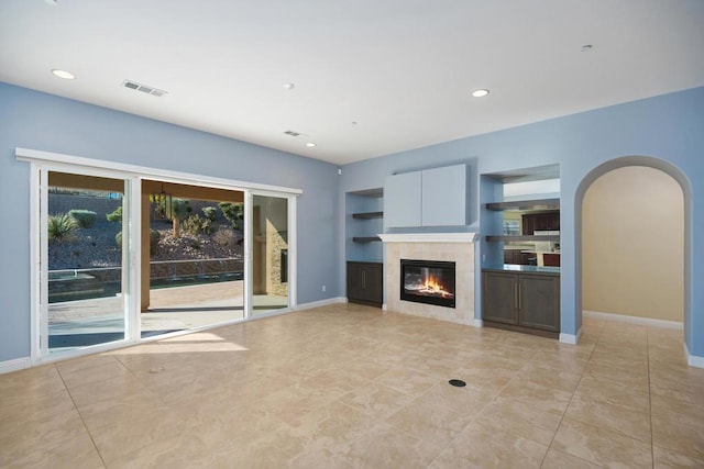 unfurnished living room featuring built in shelves and a tiled fireplace