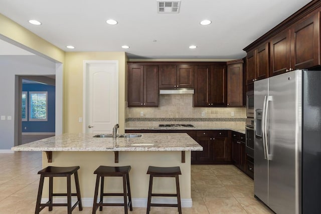 kitchen featuring appliances with stainless steel finishes, backsplash, sink, a center island with sink, and a breakfast bar area