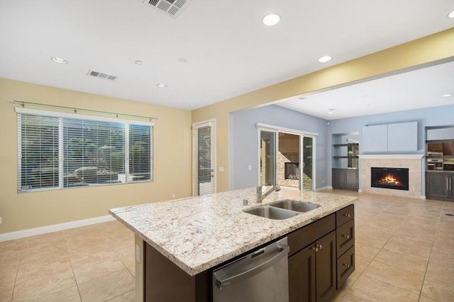 kitchen with dishwasher, a kitchen island with sink, sink, light stone countertops, and a fireplace