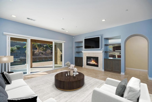 living room with built in shelves, a fireplace, and light tile patterned floors