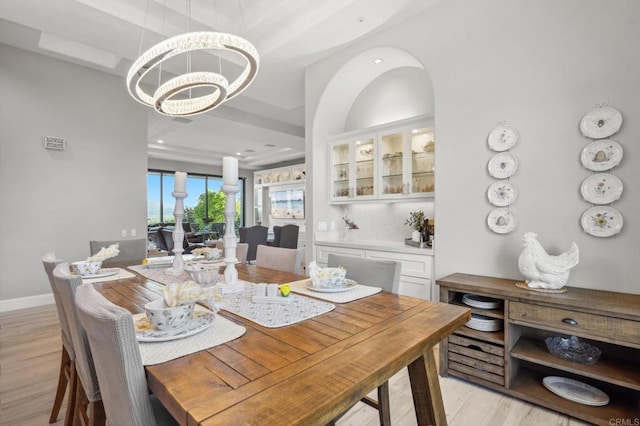 dining space with a raised ceiling, light hardwood / wood-style flooring, and a notable chandelier