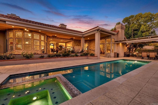 pool at dusk featuring a patio area and an in ground hot tub