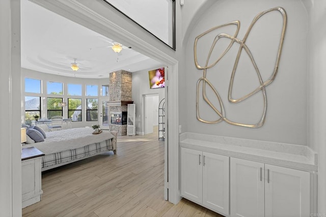 bedroom featuring ceiling fan, light hardwood / wood-style floors, a raised ceiling, and a fireplace