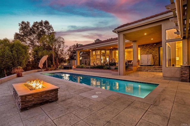 pool at dusk featuring a fire pit and a patio area