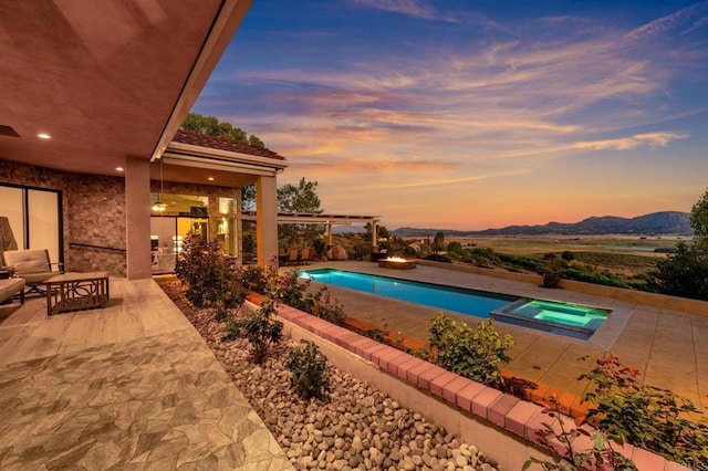 pool at dusk with an in ground hot tub, a mountain view, and a patio