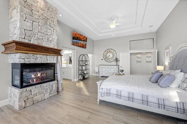 bedroom featuring ceiling fan, light wood-type flooring, a fireplace, a towering ceiling, and a tray ceiling