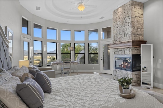 bedroom featuring a tray ceiling, a stone fireplace, ceiling fan, and a high ceiling