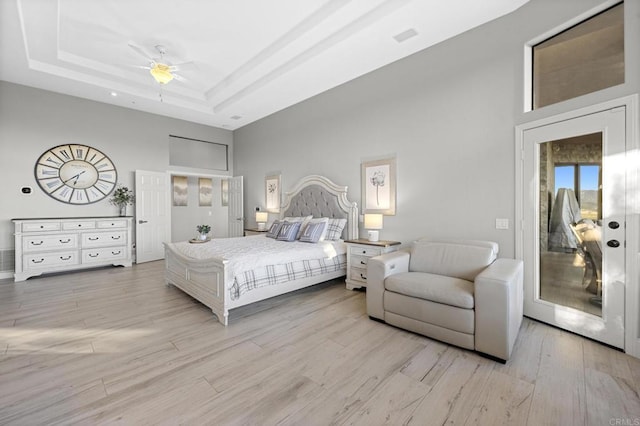 bedroom with access to outside, ceiling fan, a towering ceiling, a tray ceiling, and light hardwood / wood-style floors