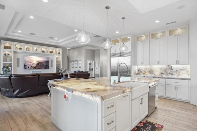 kitchen featuring sink, stainless steel appliances, a tray ceiling, a kitchen island with sink, and white cabinets