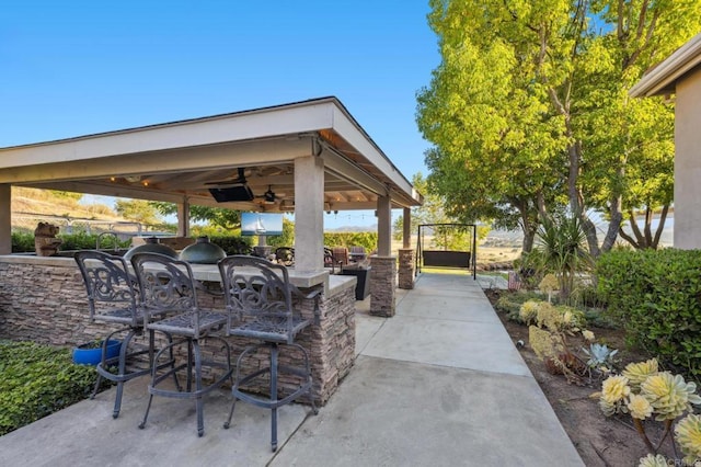 view of patio featuring a gazebo, ceiling fan, a bar, and exterior kitchen