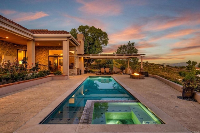 pool at dusk with an in ground hot tub, an outdoor fire pit, and a patio area