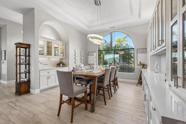 dining room featuring light wood-style flooring, baseboards, and a tray ceiling