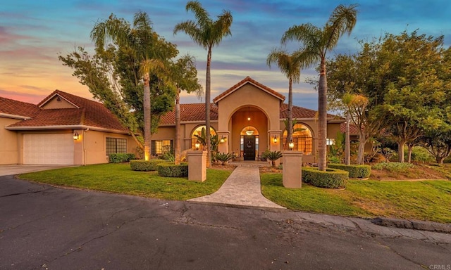 mediterranean / spanish house with driveway, an attached garage, a yard, stucco siding, and a tiled roof