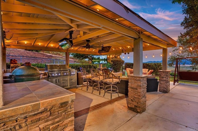 view of patio featuring a ceiling fan, fence, an outdoor kitchen, a gazebo, and a grill