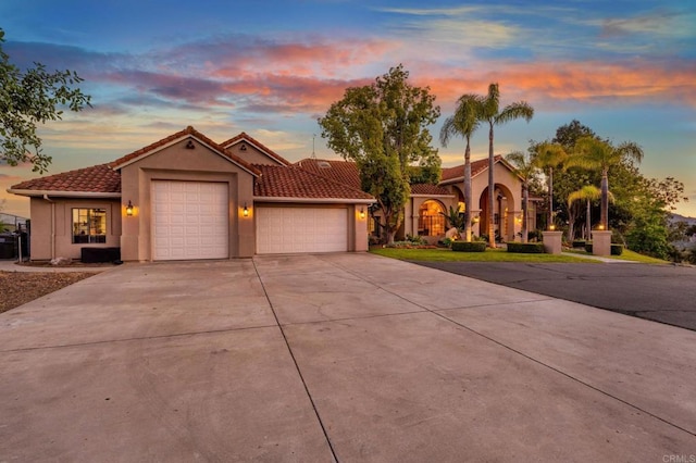 mediterranean / spanish-style home featuring concrete driveway, an attached garage, a tile roof, and stucco siding