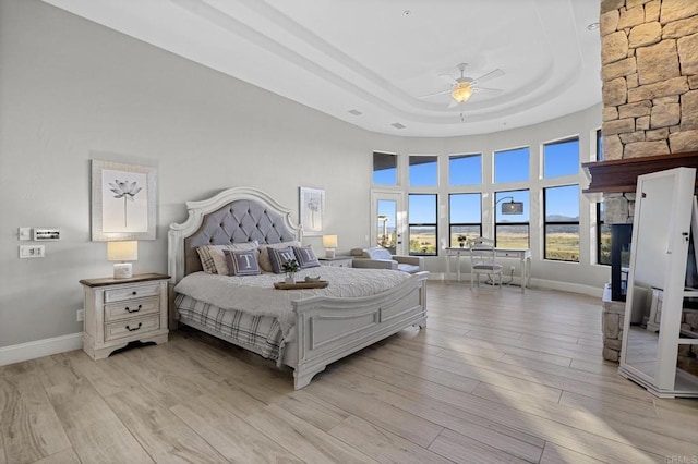 bedroom featuring light wood-type flooring, a tray ceiling, a high ceiling, a fireplace, and baseboards