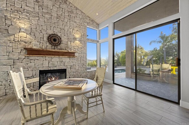 dining space with a fireplace, high vaulted ceiling, wooden ceiling, and wood finished floors