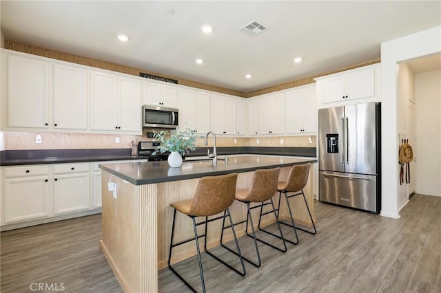 kitchen featuring sink, an island with sink, appliances with stainless steel finishes, light hardwood / wood-style floors, and white cabinetry