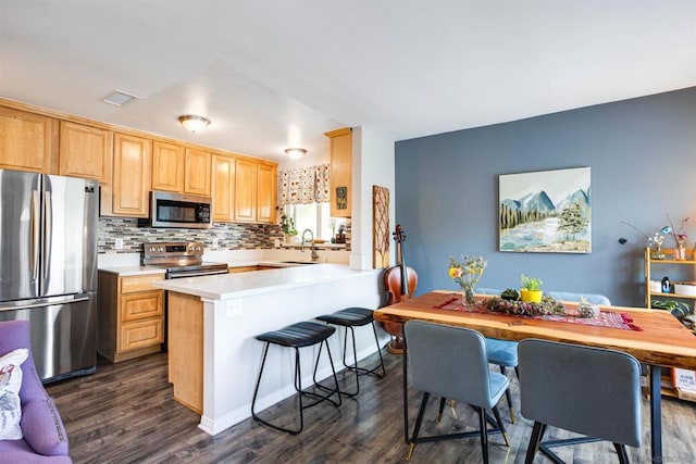 kitchen featuring kitchen peninsula, dark hardwood / wood-style floors, tasteful backsplash, appliances with stainless steel finishes, and sink