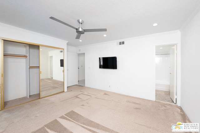 unfurnished bedroom featuring ceiling fan, crown molding, ensuite bathroom, carpet floors, and a closet