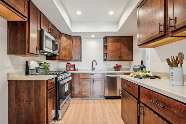 kitchen with dark brown cabinetry, appliances with stainless steel finishes, sink, a tray ceiling, and light hardwood / wood-style flooring