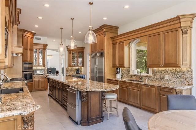 kitchen with backsplash, sink, appliances with stainless steel finishes, a kitchen island, and light stone counters