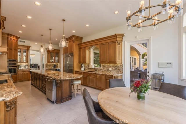 kitchen with pendant lighting, a large island with sink, decorative backsplash, light stone countertops, and appliances with stainless steel finishes