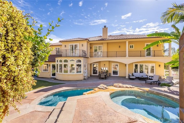 rear view of house with outdoor lounge area, a swimming pool with hot tub, a balcony, and a patio