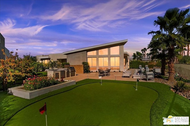 back house at dusk featuring a patio area and an outdoor kitchen