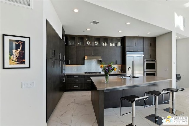 kitchen with appliances with stainless steel finishes, decorative backsplash, a center island with sink, and a breakfast bar