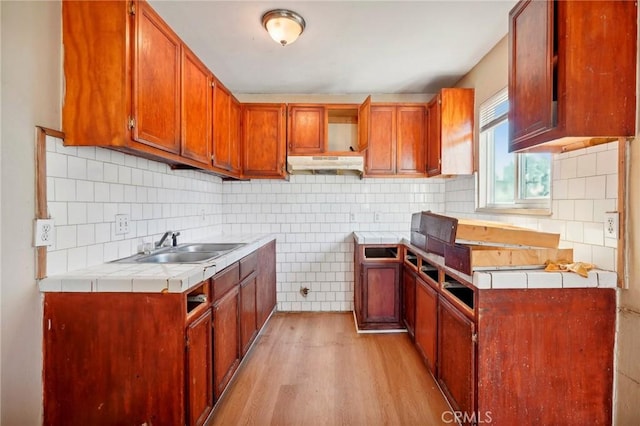 kitchen featuring tile countertops, decorative backsplash, light wood-type flooring, and sink