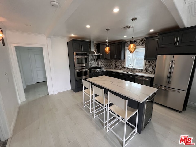 kitchen featuring wall chimney exhaust hood, light stone counters, decorative light fixtures, a kitchen island, and appliances with stainless steel finishes