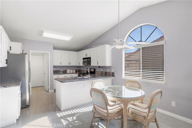 kitchen featuring kitchen peninsula, dark stone counters, stainless steel appliances, ceiling fan, and white cabinetry