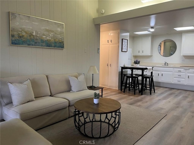 living room with wooden walls, sink, and light wood-type flooring