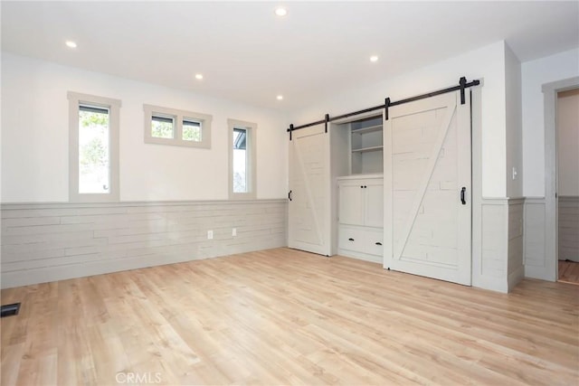 unfurnished bedroom with light hardwood / wood-style flooring and a barn door