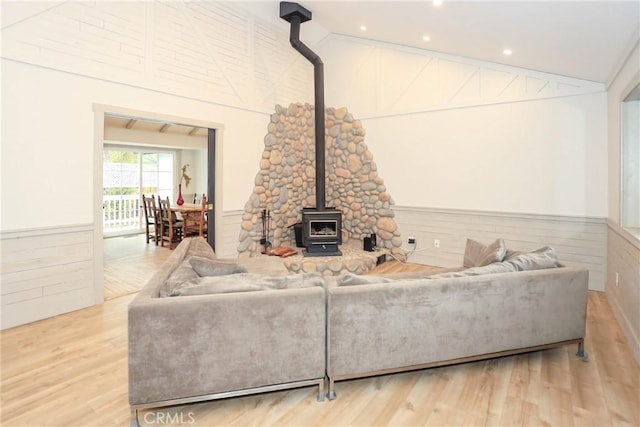 living room featuring a wood stove, light hardwood / wood-style flooring, and vaulted ceiling