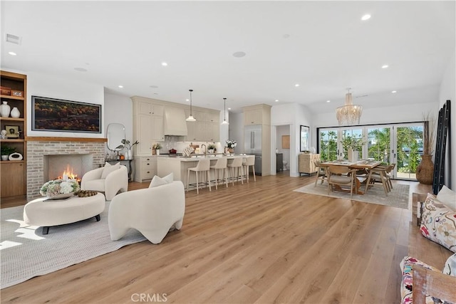 living room with sink, an inviting chandelier, light hardwood / wood-style floors, and a brick fireplace