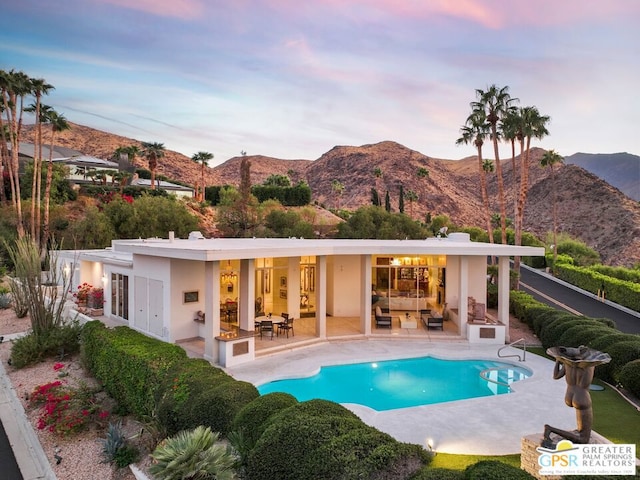 pool at dusk featuring a mountain view, french doors, a patio, and an outdoor hangout area